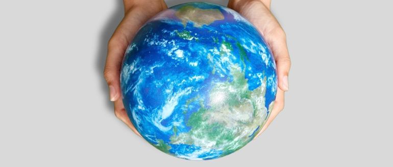 Two hands holding a globe in front of a grey background