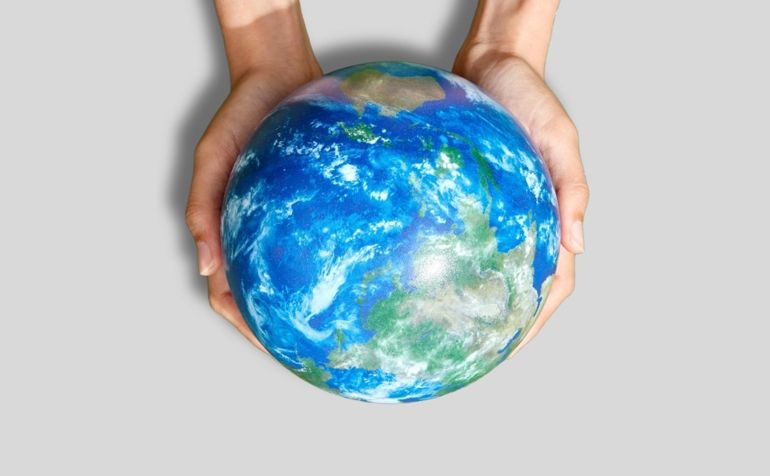 Two hands holding a globe in front of a grey background