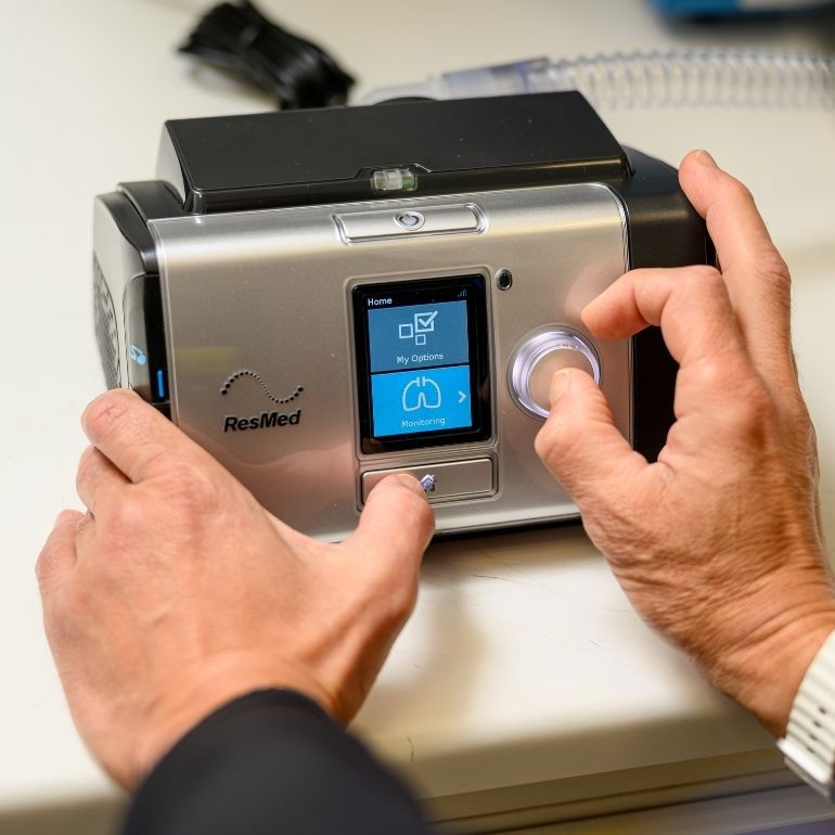 Close-up of a RESMED CPAP device and a clinician's hands turning the device on.